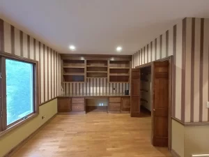 Amherst NY home office pre-remodel with striped wallpaper, built-in wood desk, open shelving, and walk-in closet.