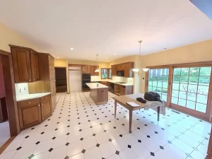 Amherst NY kitchen pre-remodel with wood cabinets, center island, tile flooring, and sliding glass doors to backyard patio.