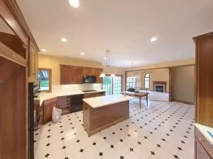 Amherst NY kitchen pre-remodel with center island, recessed lighting, wood cabinetry, and open flow to living room.