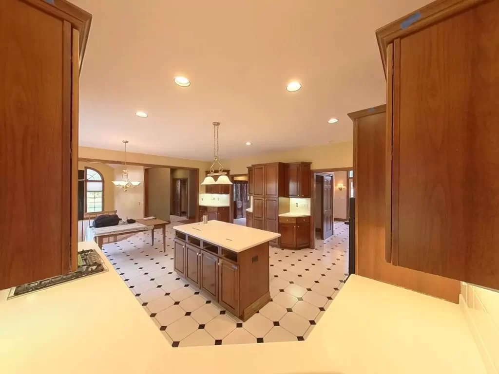 Amherst NY kitchen pre-remodel view with center island, wood cabinetry, recessed lighting, and open layout to dining area.