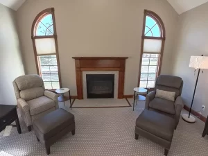 Amherst NY living room remodel with updated fireplace surround, neutral paint, and paired accent chairs by arched windows.