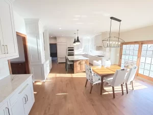 Amherst NY kitchen remodel with white cabinetry, quartz countertops, center island, wood floors, and dining area with patio doors.