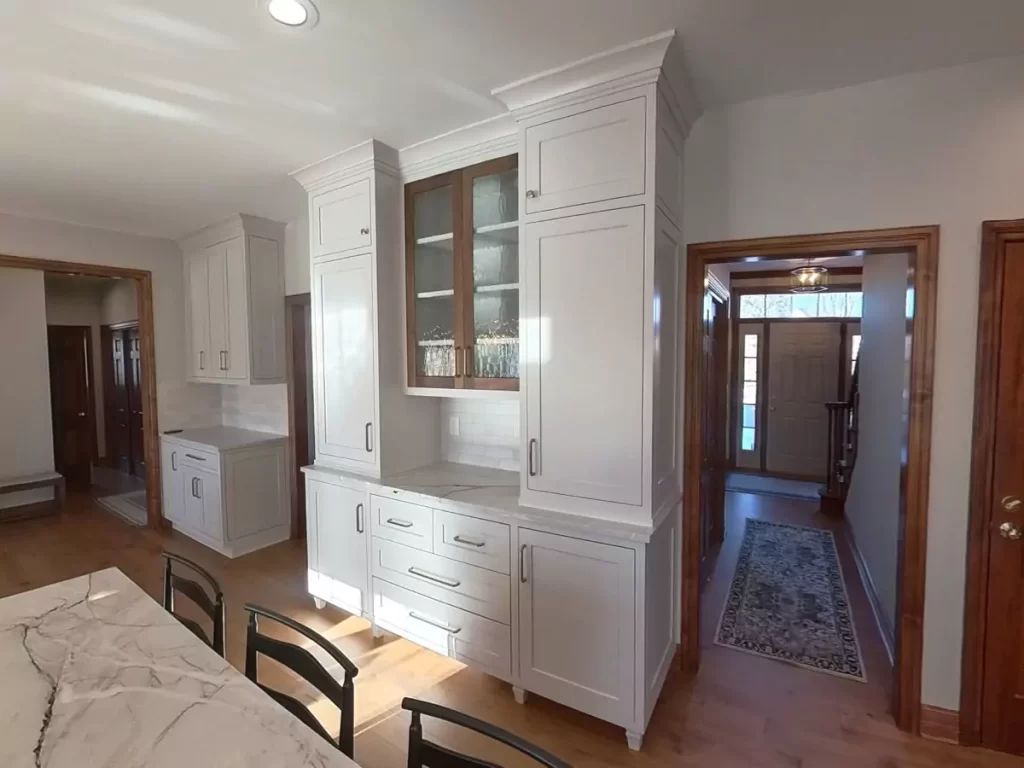 Amherst NY kitchen remodel with built-in glass display cabinet, white shaker cabinetry, and quartz countertops near entry hall.