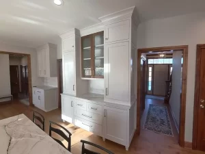 Amherst NY kitchen remodel with built-in glass display cabinet, white shaker cabinetry, and quartz countertops near entry hall.