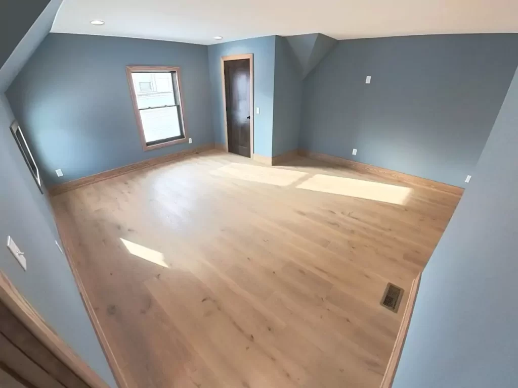 Light-filled bonus room with wide-plank hardwood floors, dark wood door, and custom trim in Buffalo home expansion project.