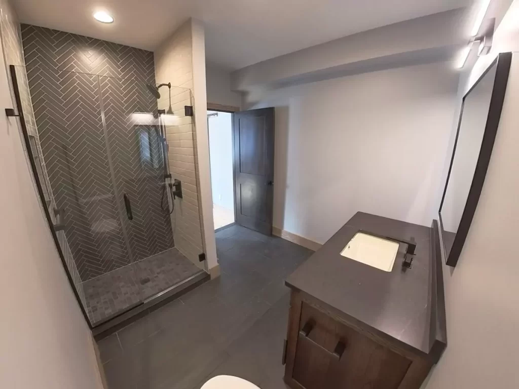 Modern bathroom with herringbone tile shower, glass enclosure, quartz vanity top, and matte black fixtures in Buffalo remodel.