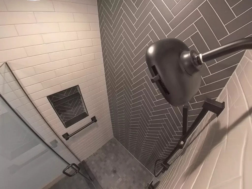 Close-up of matte black shower fixtures, herringbone tile niche, and contrasting subway tile in modern Buffalo bathroom remodel.
