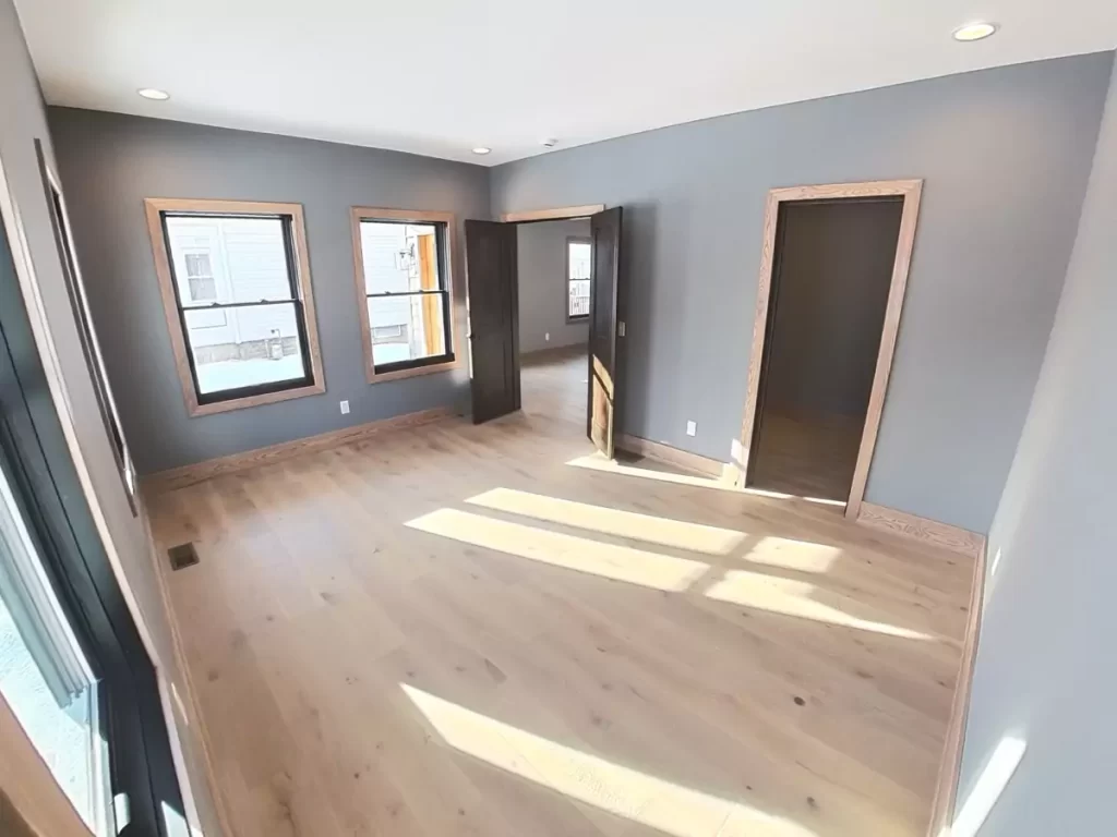 Sunlit bedroom with hardwood floors, dual windows, and natural wood trim in Buffalo home addition project.