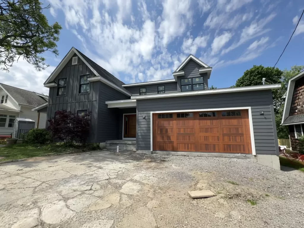 Buffalo home addition with modern gray siding, wood garage door, and second-story expansion under a bright summer sky.