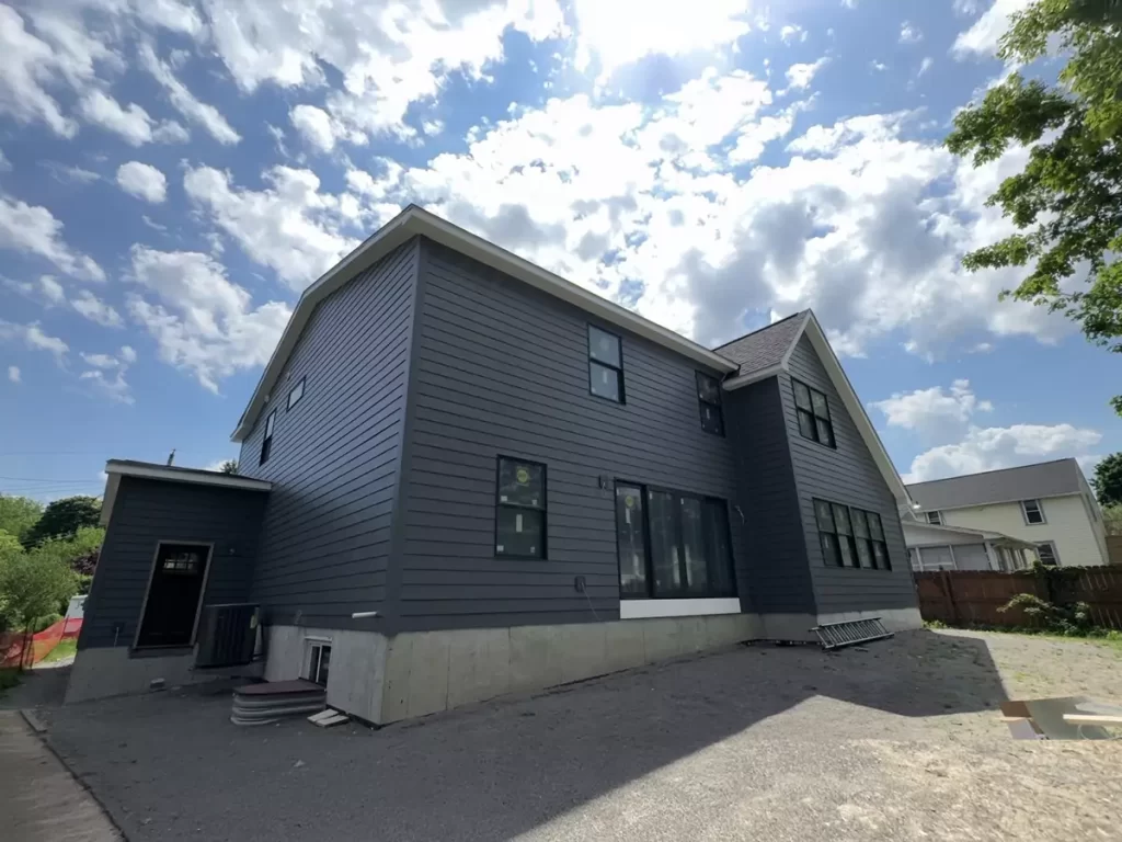 Rear view of Buffalo home addition featuring new gray siding, energy-efficient windows, and fresh concrete foundation work.