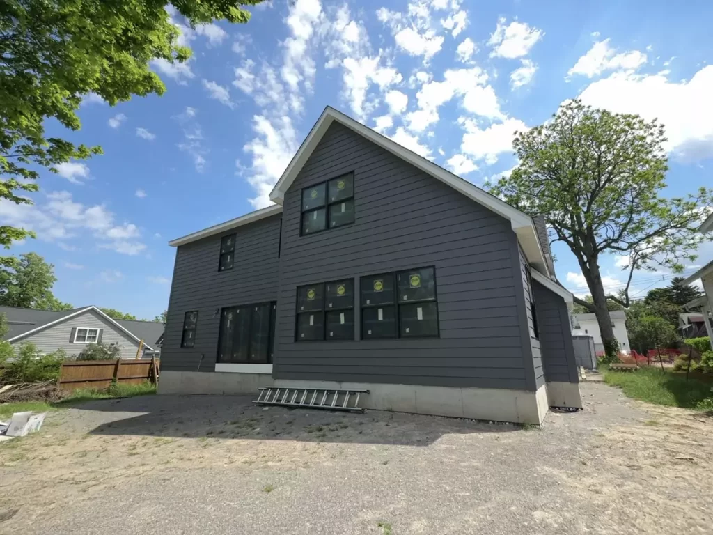 Angled rear view of Buffalo home addition with new gray Hardie siding, large black-framed windows, and poured concrete base.