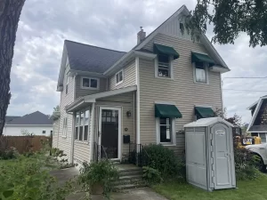 Front view of original home before renovation, with beige siding, green awnings, and visible construction prep in Buffalo, NY.