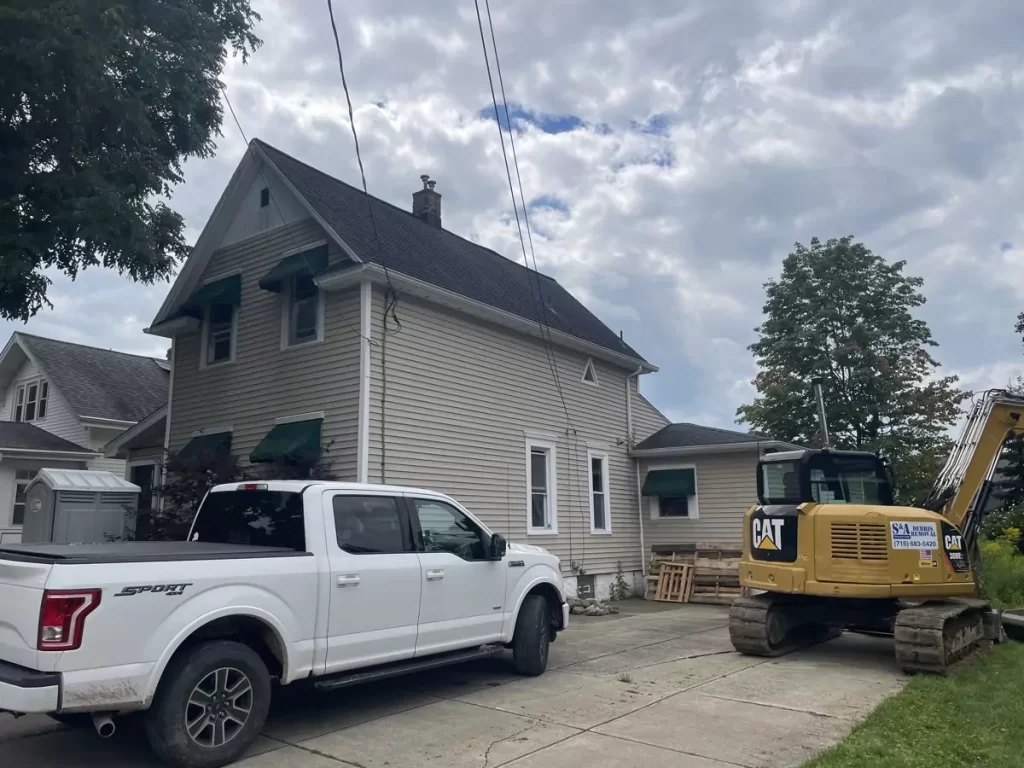 Side view of home before renovation with construction equipment and vehicles on-site in preparation for Buffalo home addition.