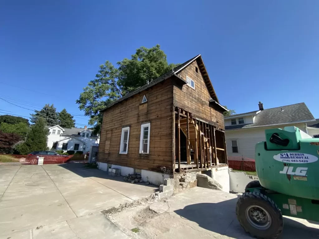 Corner view of home mid-demolition with exposed framing and debris removal equipment on-site in Buffalo project.