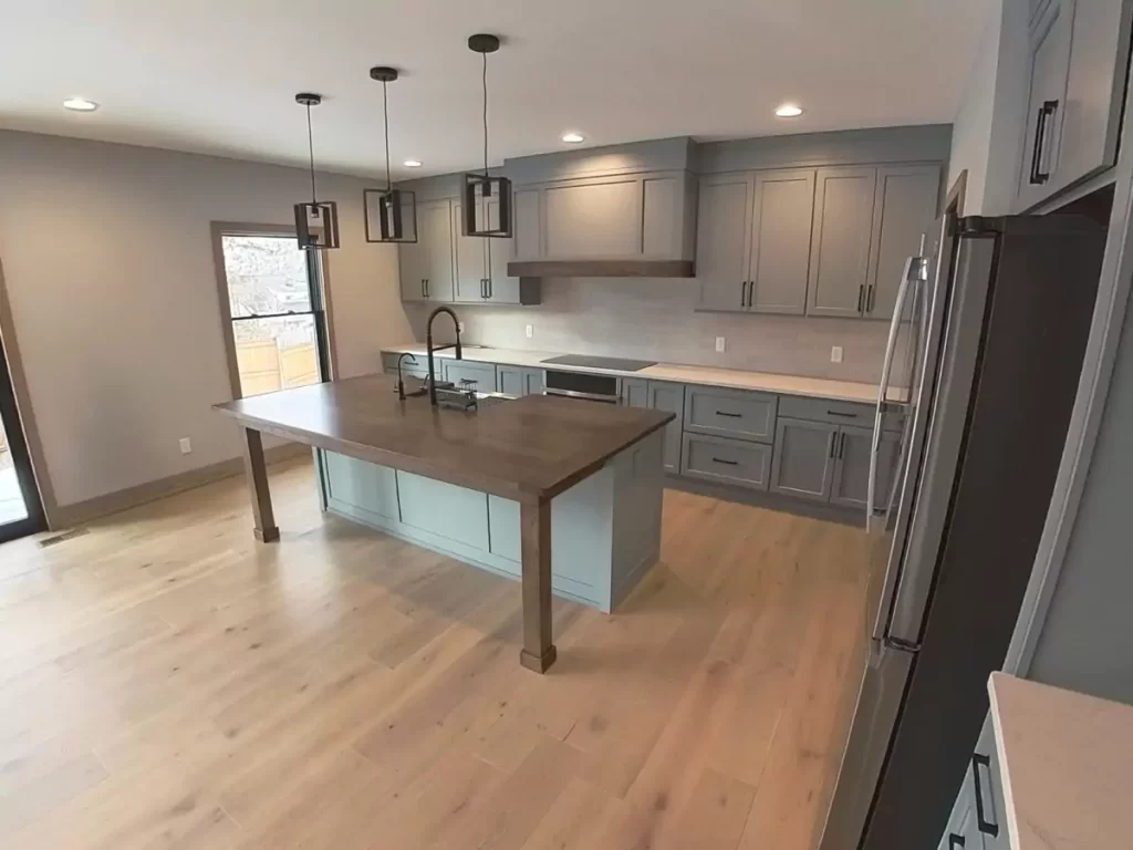 Modern kitchen with shaker cabinets, large wood island, pendant lighting, and wide-plank flooring in Buffalo custom renovation.