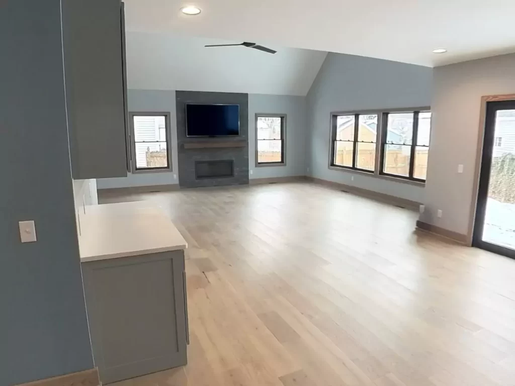 Spacious living area with stone fireplace, mounted TV, light hardwood floors, and panoramic windows in Buffalo home addition.