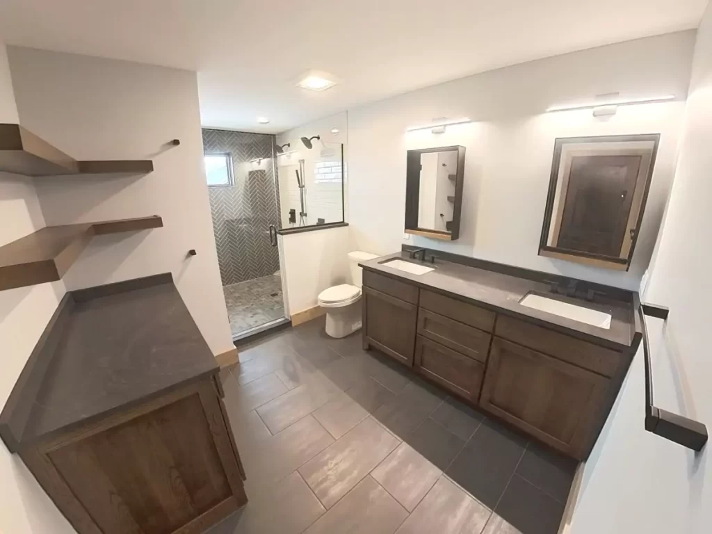 Primary bathroom with double vanity, quartz counters, walk-in shower, and herringbone tile accent in Buffalo custom home.