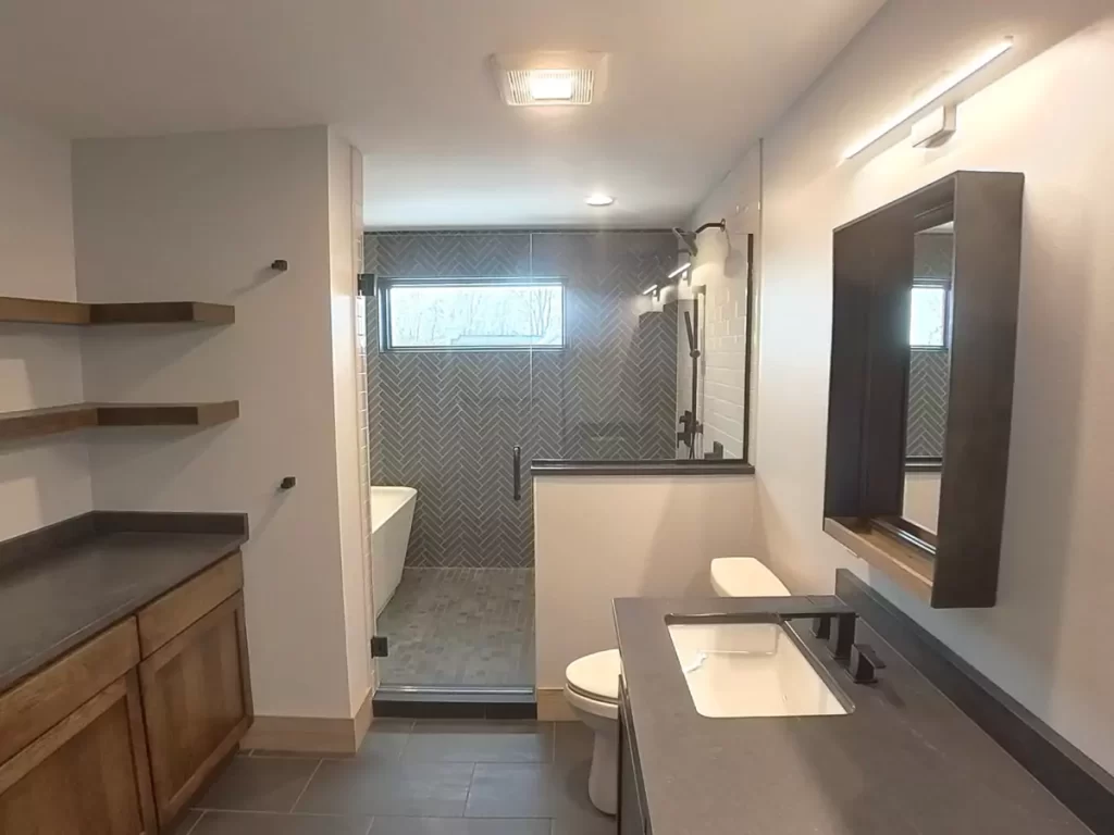 Modern primary bathroom with floating shelves, dark quartz vanity, walk-in shower, and herringbone tile in Buffalo renovation.