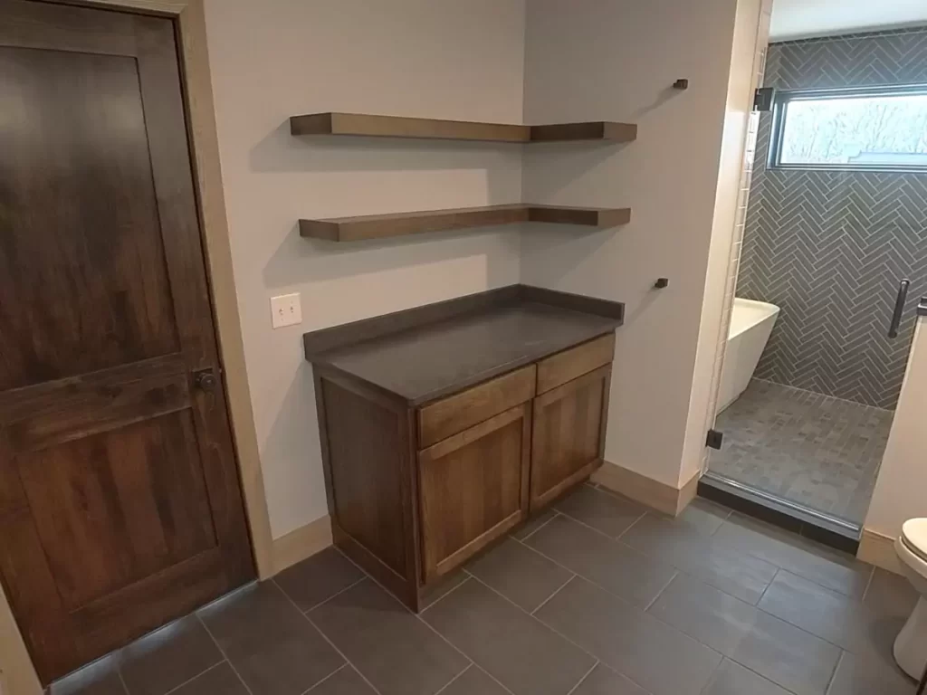 Vanity nook with quartz countertop, floating wood shelves, and access to tiled walk-in shower in Buffalo primary bathroom.