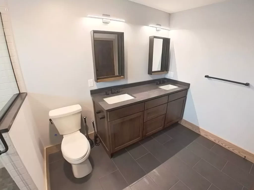 Double-sink vanity with dark quartz countertops, modern mirrors, and matte black fixtures in Buffalo primary bathroom remodel.