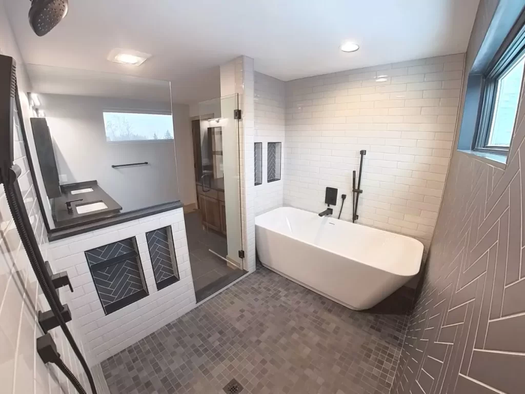 Luxury wet room with freestanding tub, glass shower, dual vanities, and herringbone tile in Buffalo primary suite renovation.