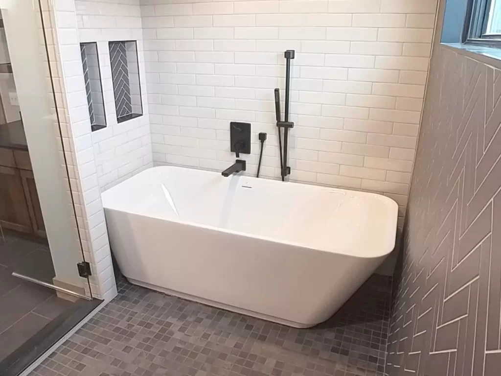 Freestanding soaking tub with matte black fixtures, herringbone tile accents, and built-in niches in Buffalo luxury bathroom.