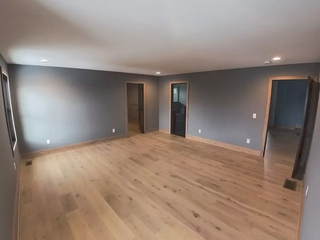 Spacious primary bedroom with wide-plank oak floors and rich gray walls in Buffalo home renovation.