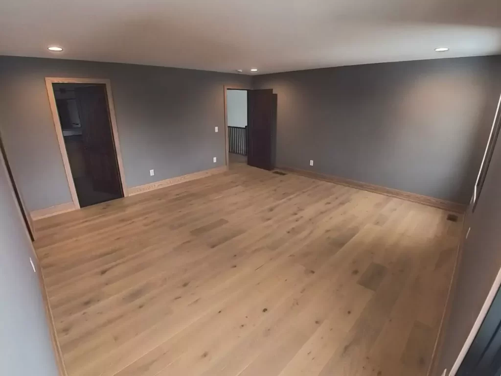 Primary bedroom with oak flooring, recessed lighting, and connected access to bath and bonus room in Buffalo remodel.
