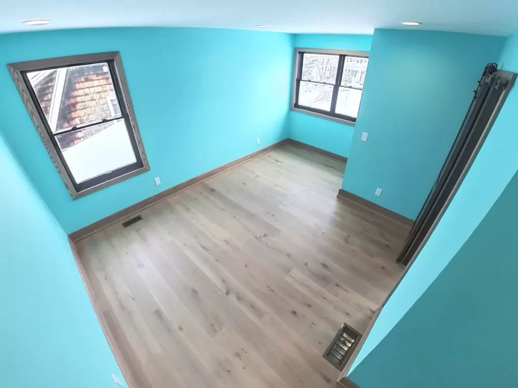 Bright bedroom with turquoise walls, light hardwood flooring, recessed lighting, and two windows providing natural light.