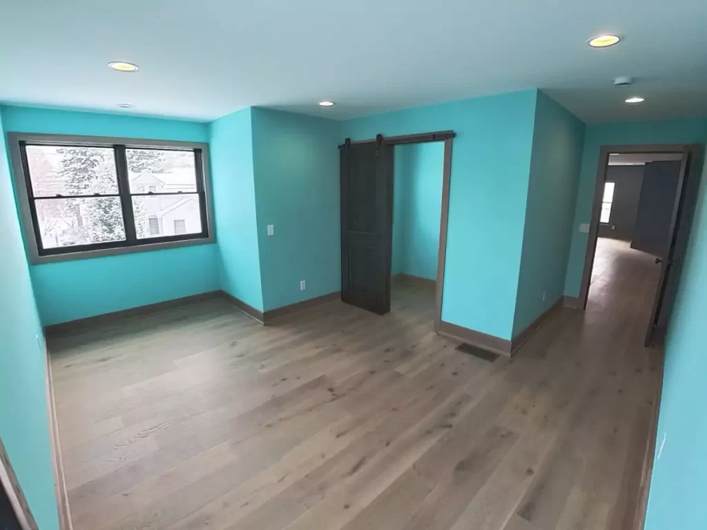 Secondary bedroom in home addition featuring turquoise walls, wide-plank hardwood flooring, recessed lighting, and a sliding barn door leading to closet or ensuite space.