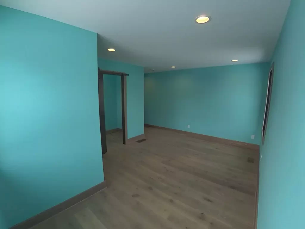 Long turquoise-walled bedroom from second-floor addition with recessed lighting and hardwood floors in custom home remodel.