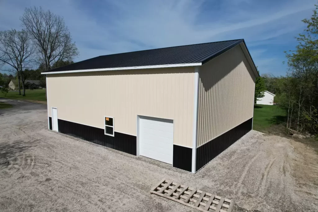 Angled side view of post-frame garage with black metal wainscoting and white overhead door in suburban Amherst NY.