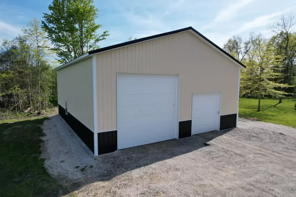 Front view of cream and black pole barn garage with dual overhead doors, surrounded by trees in Amherst NY.