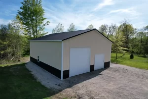 Corner view of custom post-frame garage with black metal roof and dual overhead doors in wooded Amherst NY setting.