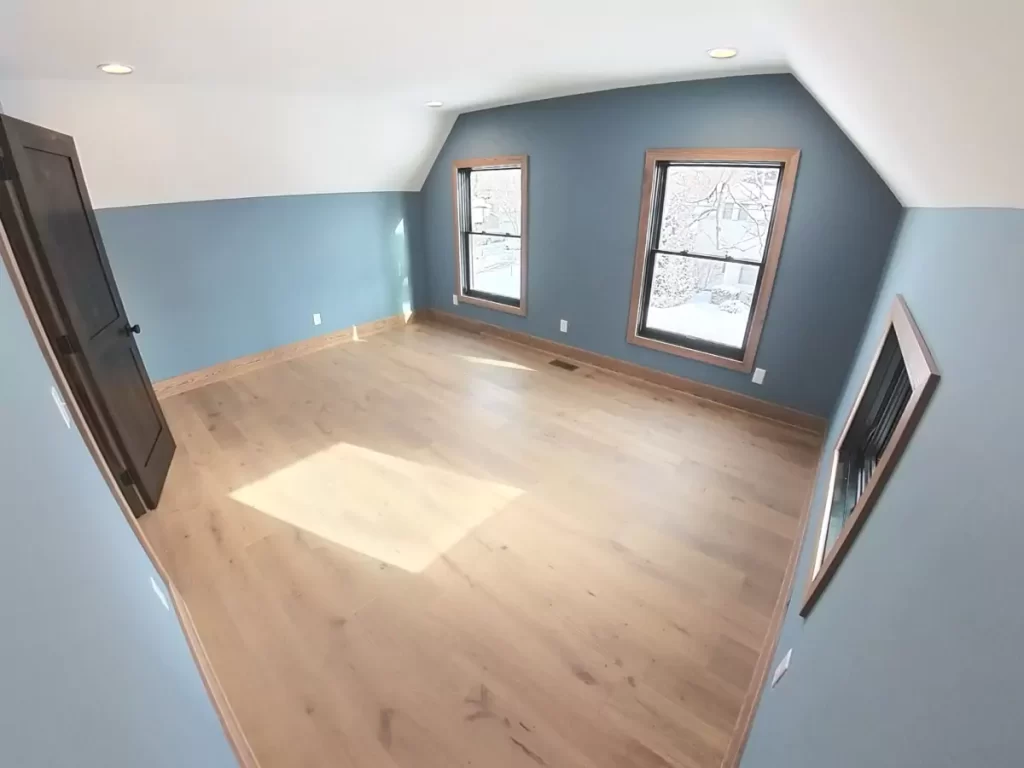 Upstairs bedroom in Buffalo home addition featuring angled ceilings, blue accent walls, and natural light from double front-facing windows.