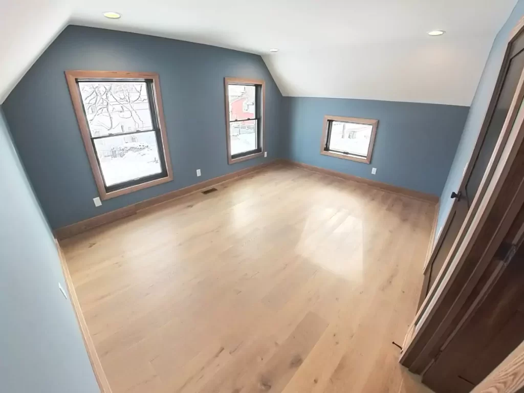 Top-floor bedroom from Buffalo home remodel featuring natural light, blue walls, and hardwood floors added during the renovation project.