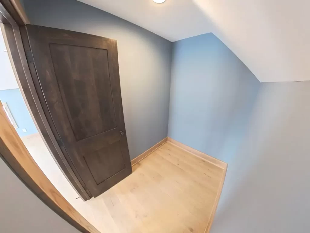 Newly finished walk-in closet with sloped ceiling in Buffalo attic bedroom remodel, featuring soft blue walls and hardwood floors.