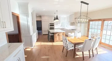 Amherst NY kitchen remodel with white cabinetry, quartz countertops, center island, wood floors, and dining area with patio doors.