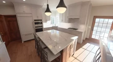 Amherst NY kitchen remodel with marble-look island, white shaker cabinets, double oven, and pendant lighting.