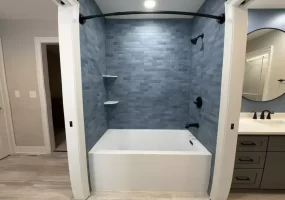 Deep bathtub and sleek blue tile surround with black fixtures by Stately Kitchen and Bath in Orchard Park, NY.
