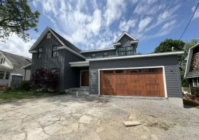 Buffalo home addition with modern gray siding, wood garage door, and second-story expansion under a bright summer sky.