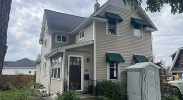Front view of original home before renovation, with beige siding, green awnings, and visible construction prep in Buffalo, NY.