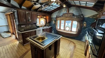 Before remodel image of a ship-themed kitchen in Elma, NY, showcasing extensive wooden cabinetry, faux ship stern, and skylights.