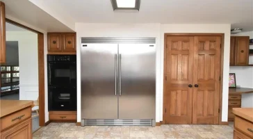 Old kitchen with large stainless steel refrigerator and wooden pantry doors.