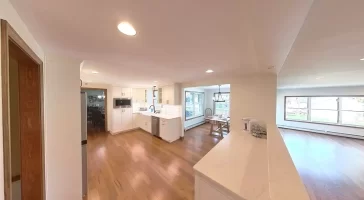 Kitchen with white cabinets, marble counters, and wood flooring, seamlessly connecting to living and dining areas for an open-concept layout.