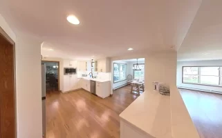 Kitchen with white cabinets, marble counters, and wood flooring, seamlessly connecting to living and dining areas for an open-concept layout.