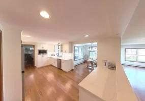 Kitchen with white cabinets, marble counters, and wood flooring, seamlessly connecting to living and dining areas for an open-concept layout.