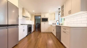 Spacious kitchen with ample natural light, featuring hardwood floors and white cabinets.