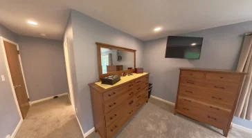 Clarence, NY home addition by Stately General Contracting, showing the primary bedroom suite with dresser, TV, and bright interior design.