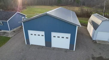 Twilight angle showcasing custom pole barn, white garage doors, and charcoal steel wainscoting.